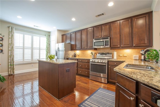 kitchen featuring visible vents, a kitchen island, light stone countertops, stainless steel appliances, and a sink