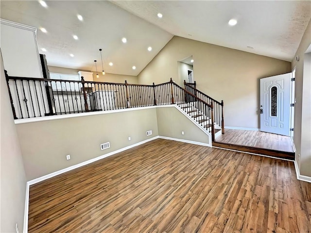 empty room with lofted ceiling, visible vents, stairway, wood finished floors, and baseboards