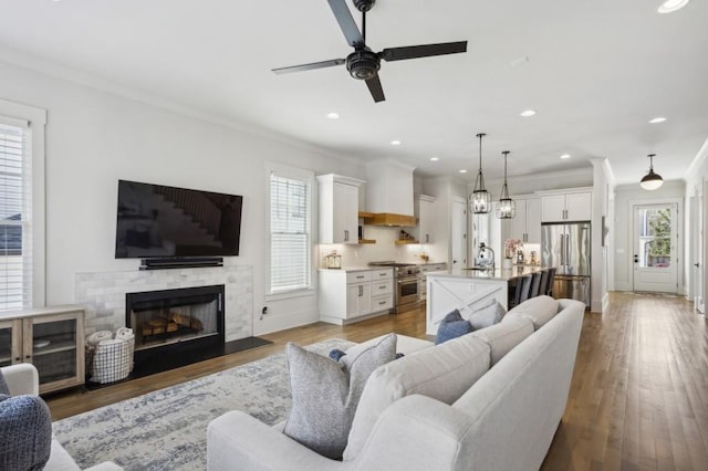 living room featuring ceiling fan with notable chandelier, light hardwood / wood-style flooring, sink, and crown molding