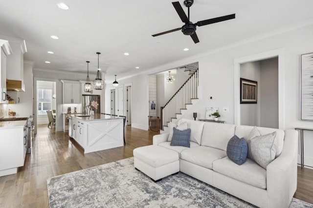 living room featuring hardwood / wood-style floors, sink, ornamental molding, and ceiling fan with notable chandelier