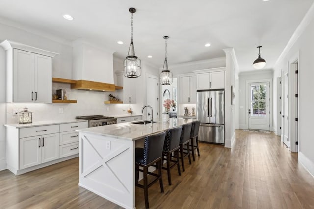 kitchen with decorative light fixtures, high end refrigerator, white cabinets, sink, and light wood-type flooring