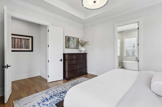 bedroom with a tray ceiling, dark hardwood / wood-style flooring, and ensuite bathroom