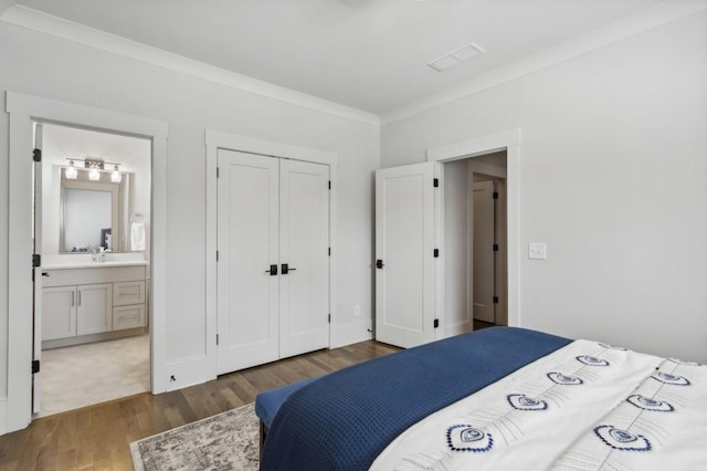 bedroom featuring a closet, connected bathroom, sink, crown molding, and dark hardwood / wood-style floors