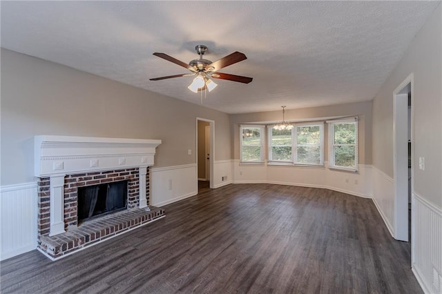 unfurnished living room featuring dark wood-type flooring, a textured ceiling, ceiling fan with notable chandelier, and a brick fireplace