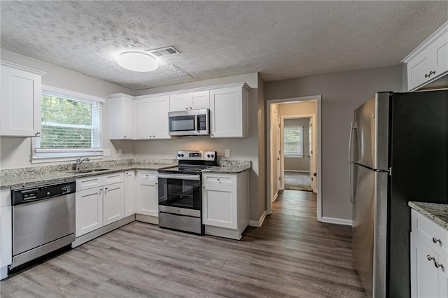 kitchen featuring white cabinets, light hardwood / wood-style flooring, a textured ceiling, light stone countertops, and appliances with stainless steel finishes