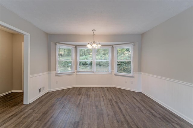 empty room featuring plenty of natural light, an inviting chandelier, and dark hardwood / wood-style flooring