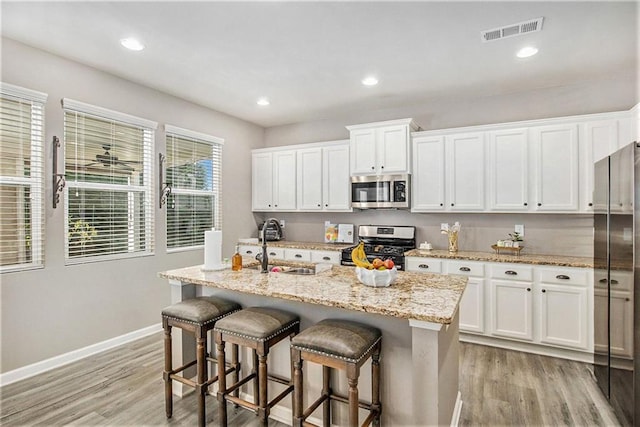 1329 Old Glory Ct, Hoschton, GA 30548 - kitchen featuring appliances with stainless steel finishes, light wood-style floors, white cabinets, a breakfast bar, and recessed lighting