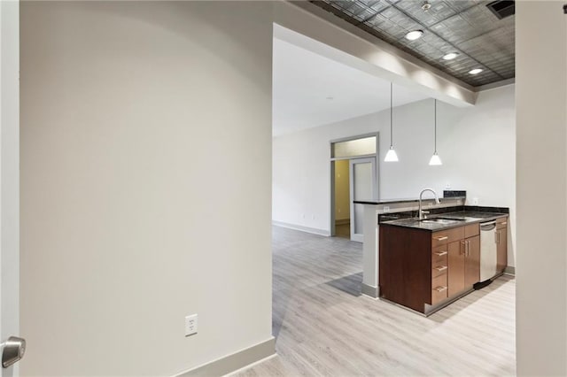 kitchen with stainless steel dishwasher, sink, decorative light fixtures, dark stone countertops, and light hardwood / wood-style floors