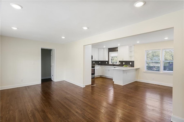 interior space with stainless steel stove, white cabinetry, backsplash, dark hardwood / wood-style flooring, and kitchen peninsula