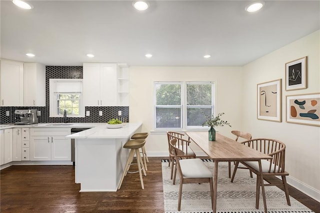 kitchen featuring dark hardwood / wood-style floors, a breakfast bar area, white cabinets, decorative backsplash, and kitchen peninsula