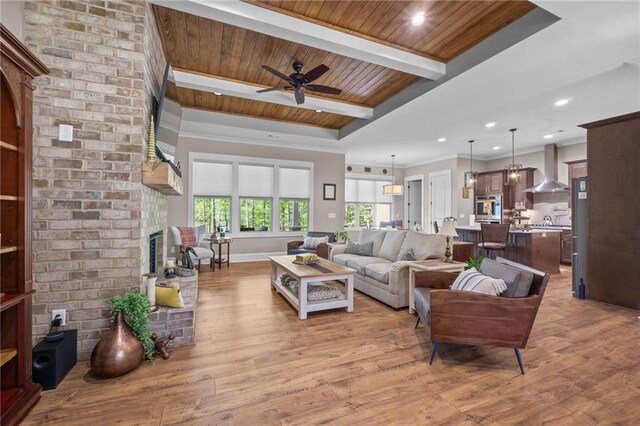 living room featuring light wood-type flooring, a fireplace, a tray ceiling, ceiling fan, and wooden ceiling