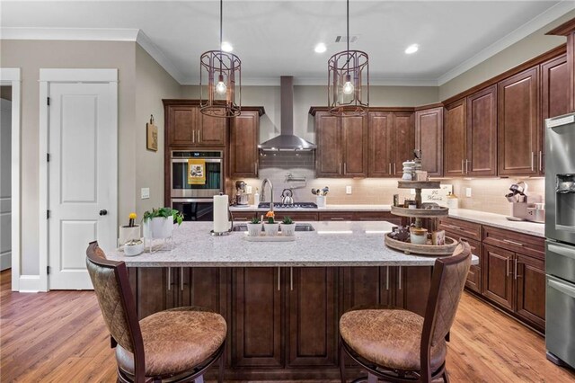 kitchen featuring stainless steel appliances, wall chimney range hood, light hardwood / wood-style flooring, and a kitchen bar