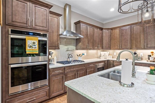 kitchen with appliances with stainless steel finishes, sink, wall chimney exhaust hood, pendant lighting, and crown molding