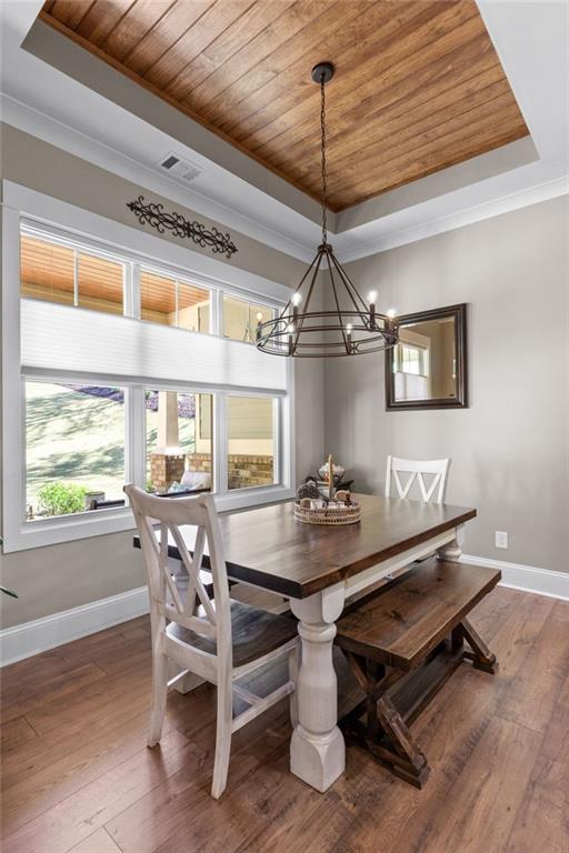 dining room with wood-type flooring, wood ceiling, a raised ceiling, crown molding, and an inviting chandelier