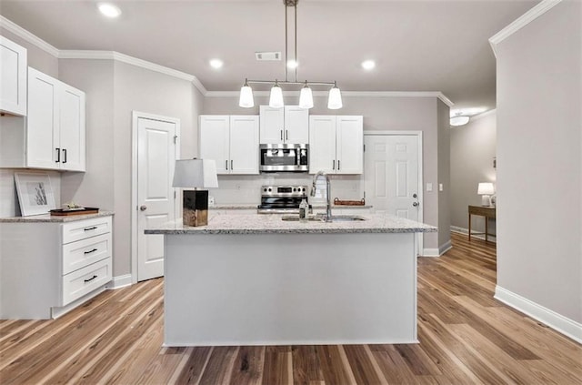 kitchen featuring appliances with stainless steel finishes, white cabinetry, sink, light stone countertops, and a center island with sink