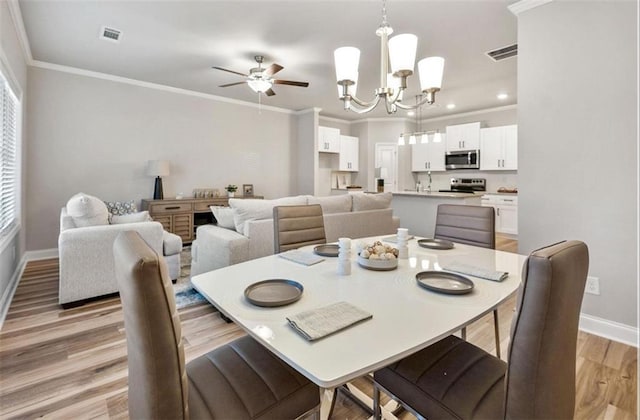 dining room with ornamental molding, ceiling fan with notable chandelier, and light hardwood / wood-style flooring