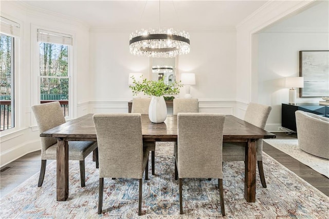 dining area featuring crown molding, a decorative wall, an inviting chandelier, wainscoting, and wood finished floors