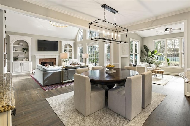 dining room with ornamental molding, lofted ceiling, a warm lit fireplace, and dark wood-style flooring