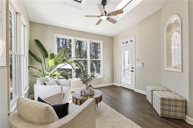 interior space featuring vaulted ceiling with skylight, dark wood finished floors, baseboards, and ceiling fan