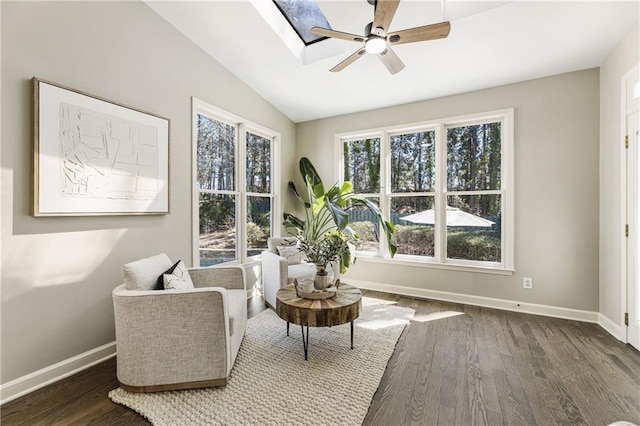 living area featuring dark wood-style floors, ceiling fan, lofted ceiling with skylight, and baseboards