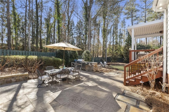 view of patio featuring outdoor dining space, a fenced backyard, stairway, and an outdoor kitchen