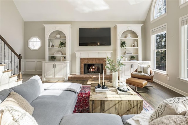 living area featuring built in shelves, vaulted ceiling, a fireplace, and plenty of natural light