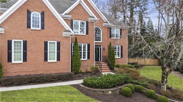 view of front of property featuring a shingled roof, fence, and brick siding