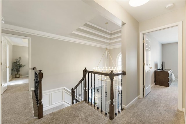 hall featuring carpet floors, a chandelier, ornamental molding, and an upstairs landing