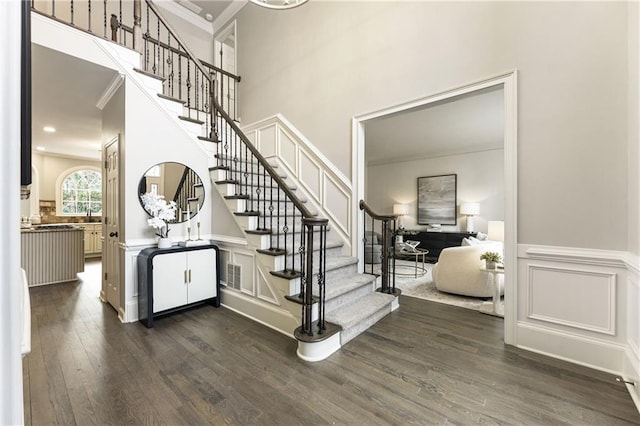 foyer with wainscoting, stairway, dark wood-type flooring, crown molding, and a decorative wall