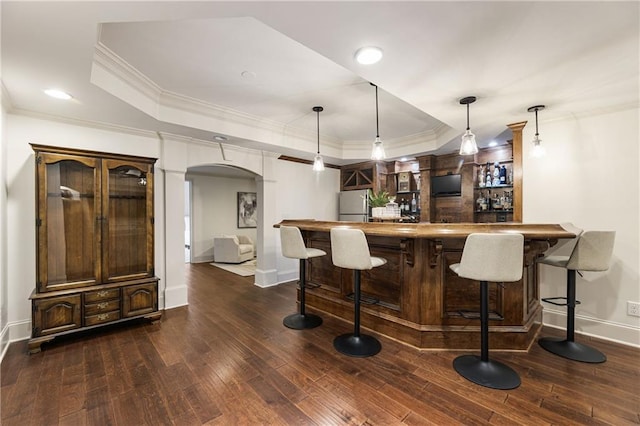 bar featuring dark wood-style floors, a tray ceiling, freestanding refrigerator, and arched walkways