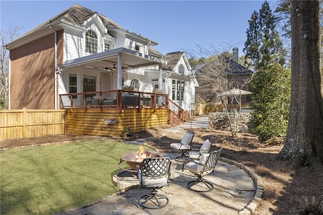 back of house featuring fence, a fire pit, a wooden deck, and a lawn