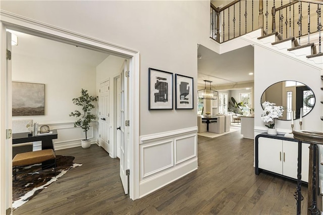 hallway featuring stairway, a decorative wall, dark wood-style flooring, and wainscoting