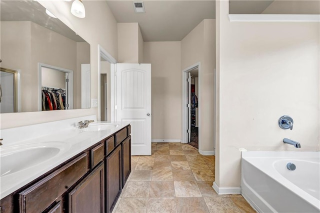 bathroom featuring a garden tub, double vanity, visible vents, a spacious closet, and a sink