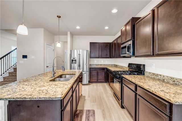 kitchen featuring appliances with stainless steel finishes, light wood-style floors, a sink, dark brown cabinets, and light stone countertops