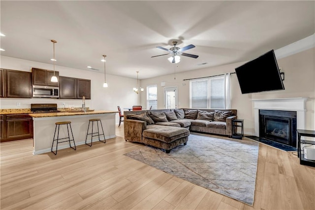 living area featuring light wood-style floors, baseboards, ceiling fan, and a fireplace with flush hearth