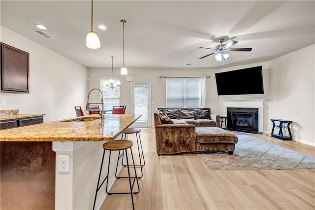 kitchen featuring light stone counters, visible vents, light wood-style flooring, a sink, and a kitchen bar