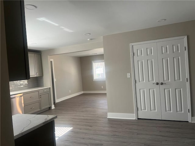 kitchen with dishwasher, gray cabinetry, backsplash, dark hardwood / wood-style flooring, and light stone counters