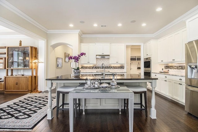 11375 Crestview Ter, Johns Creek, GA 30024 - kitchen featuring stainless steel appliances, a kitchen breakfast bar, arched walkways, white cabinets, and backsplash