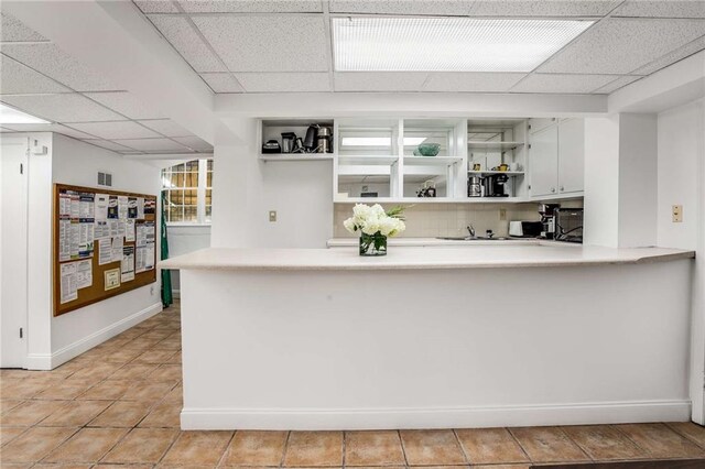 kitchen with sink, white cabinets, kitchen peninsula, a paneled ceiling, and light tile patterned floors