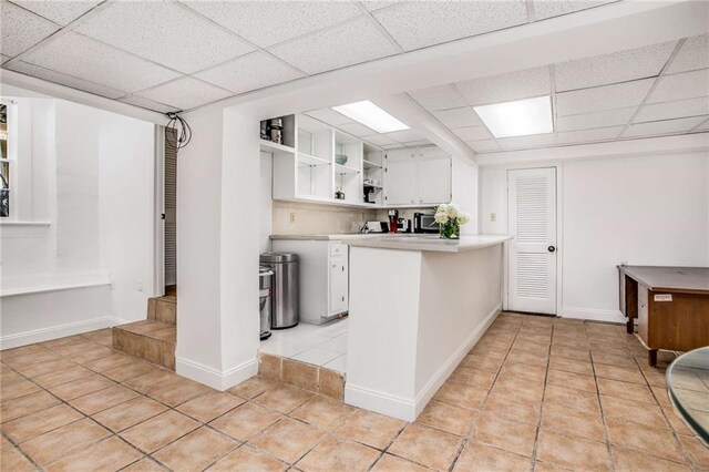 kitchen featuring light tile patterned flooring, a drop ceiling, kitchen peninsula, and white cabinetry