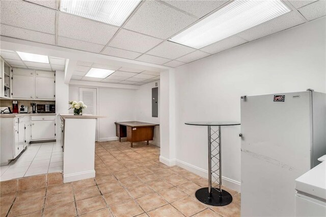 kitchen with white refrigerator, white cabinets, kitchen peninsula, light tile patterned floors, and a paneled ceiling