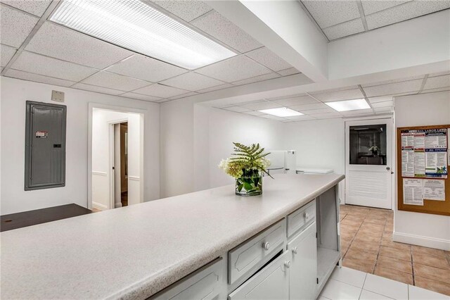 kitchen featuring electric panel, a paneled ceiling, light tile patterned floors, and white cabinetry