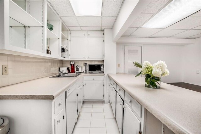 kitchen with a paneled ceiling, light tile patterned flooring, white dishwasher, and white cabinets