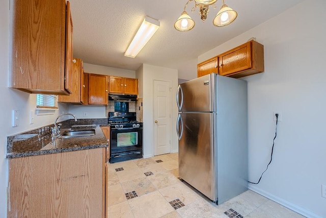 kitchen with brown cabinets, a sink, under cabinet range hood, freestanding refrigerator, and black range with gas cooktop