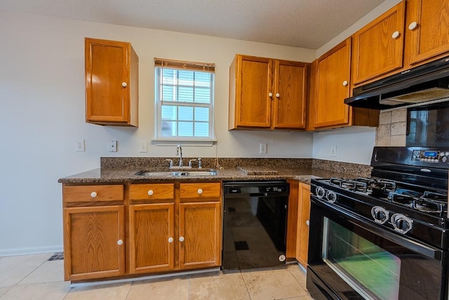 kitchen with under cabinet range hood, dark stone countertops, brown cabinetry, black appliances, and a sink