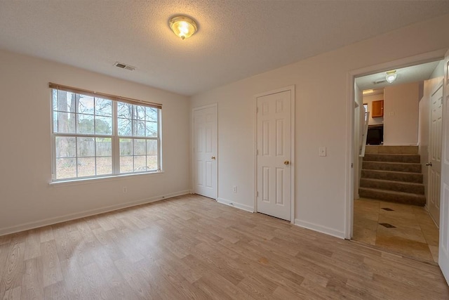 unfurnished bedroom featuring a textured ceiling, baseboards, visible vents, and light wood-type flooring