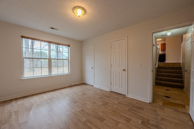 unfurnished bedroom featuring wood finished floors, baseboards, visible vents, a textured ceiling, and two closets