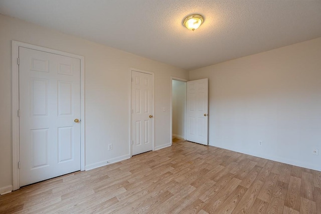 unfurnished bedroom featuring light wood-type flooring, baseboards, and a textured ceiling