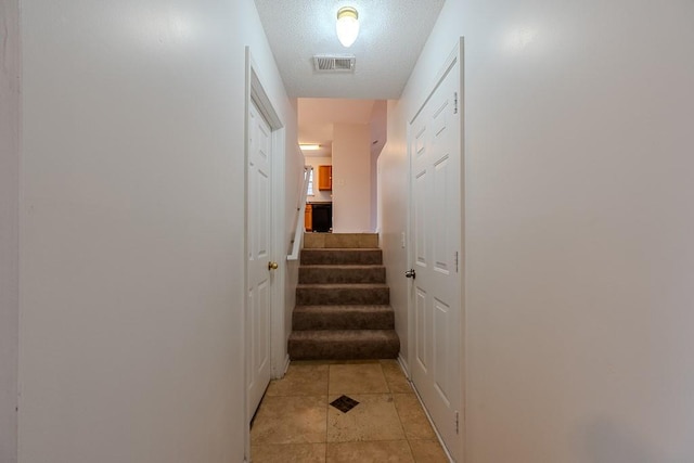 hall with light tile patterned floors, visible vents, a textured ceiling, and stairway