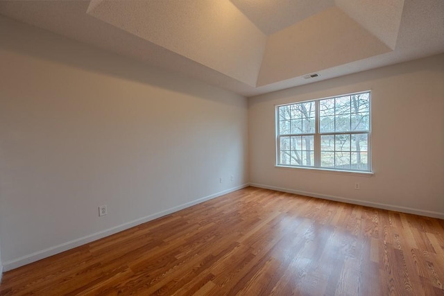 unfurnished room with a raised ceiling, wood finished floors, visible vents, and baseboards